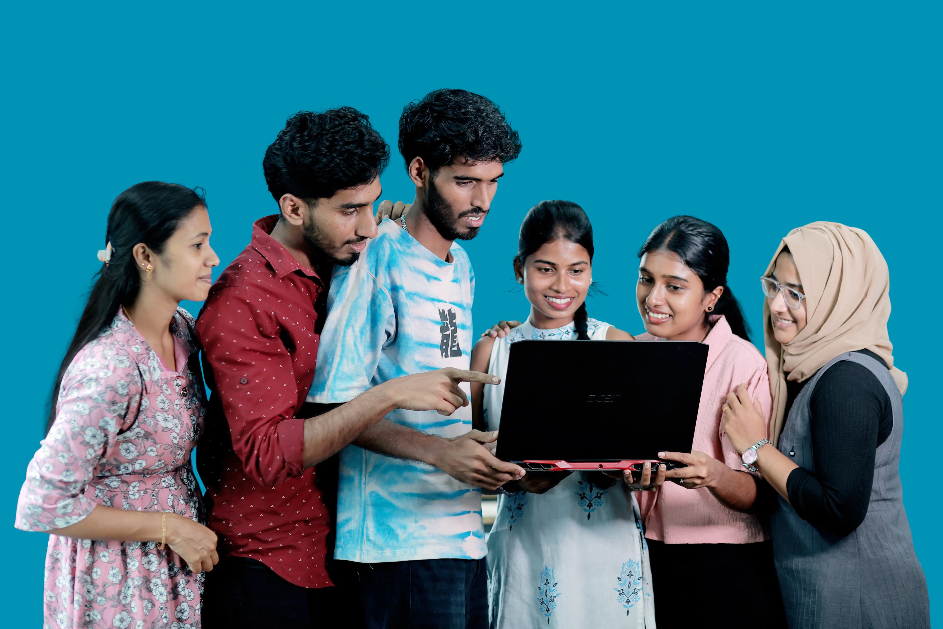 Six Plus Point students gathered around a laptop, one pointing at the screen